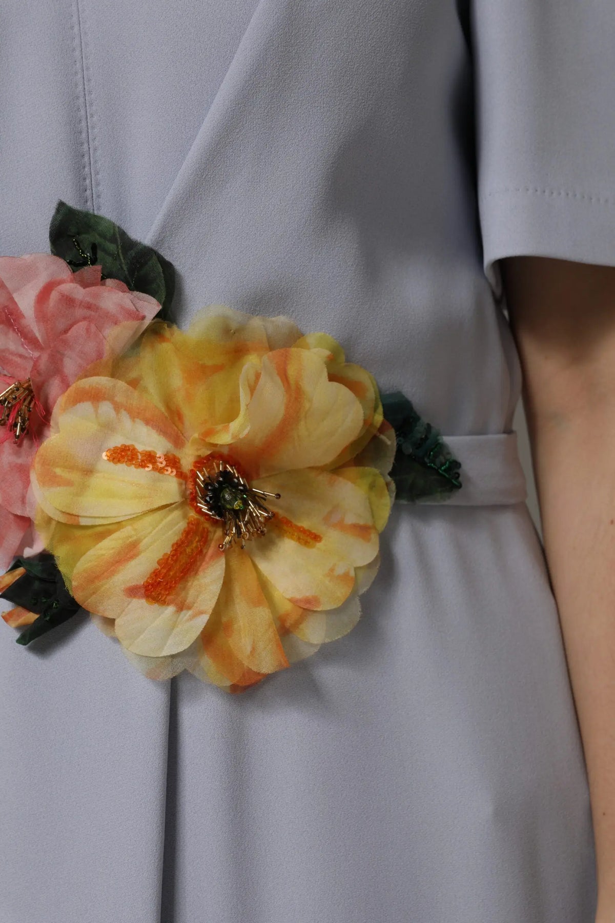 Broche florale vive jaune et orange avec pétales en tissu et feuilles vertes portée sur robe gris viscose dolce gabbana manches courtes