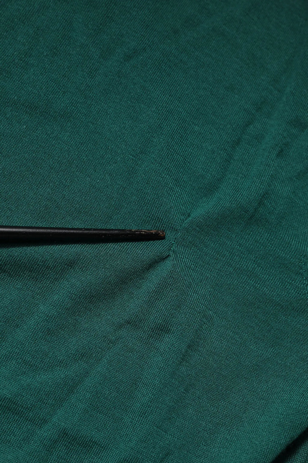 Un outil noir mince à pointe posé sur un tissu vert texturé d’un pull col rond en cachemire dolce & gabbana