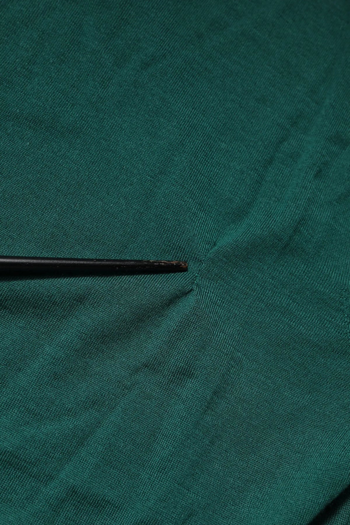 Un outil noir mince à pointe posé sur un tissu vert texturé d’un pull col rond en cachemire dolce & gabbana