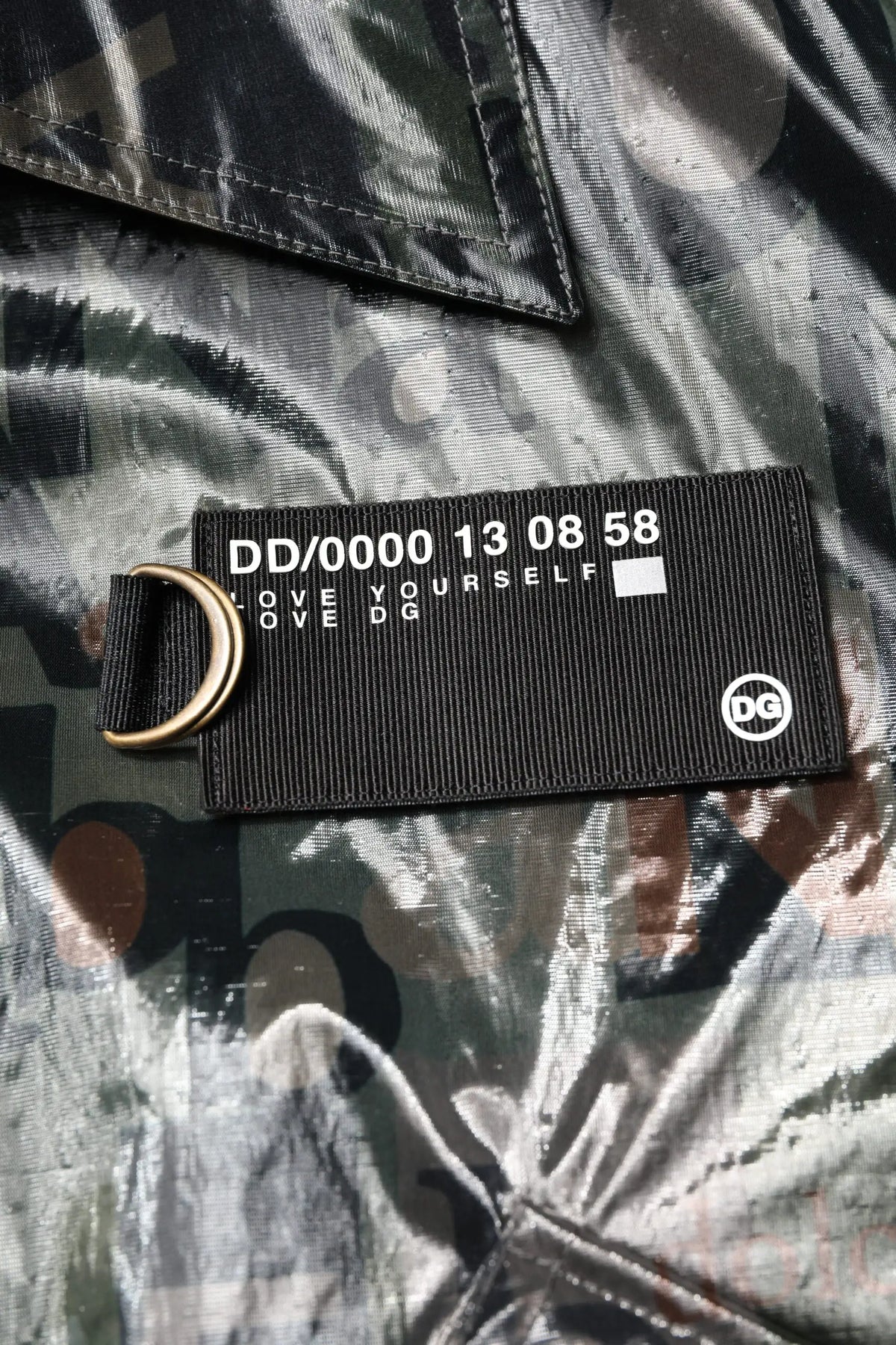 Étiquette tissée noire avec texte blanc et anneau d ou doré sur la veste bomber dolce gabbana verte à zip intégral imprimé dg