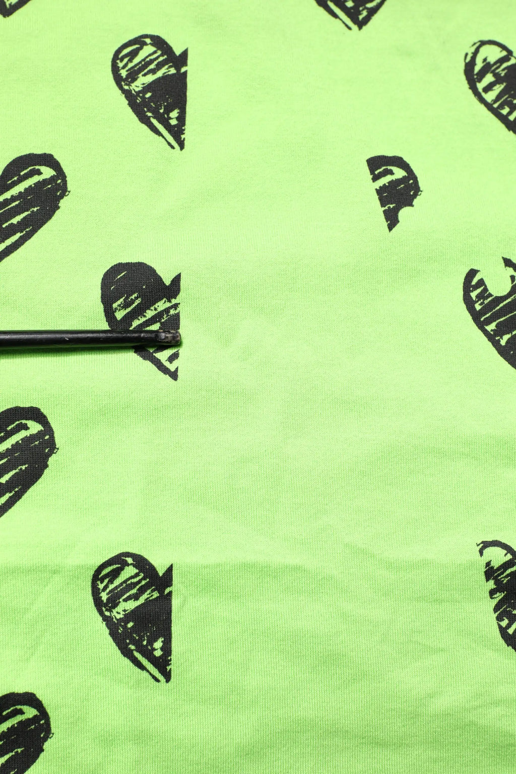 Un crayon noir posé horizontalement sur un tissu vert lime vif avec imprimé de cœurs dolce & gabbana en coton