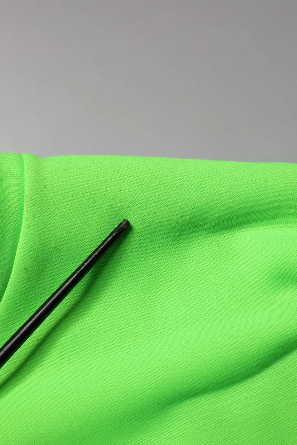 Un stylo noir élégant posé en diagonale sur un tissu vert néon du sweatshirt homme dolce & gabbana vert patchwork cœur