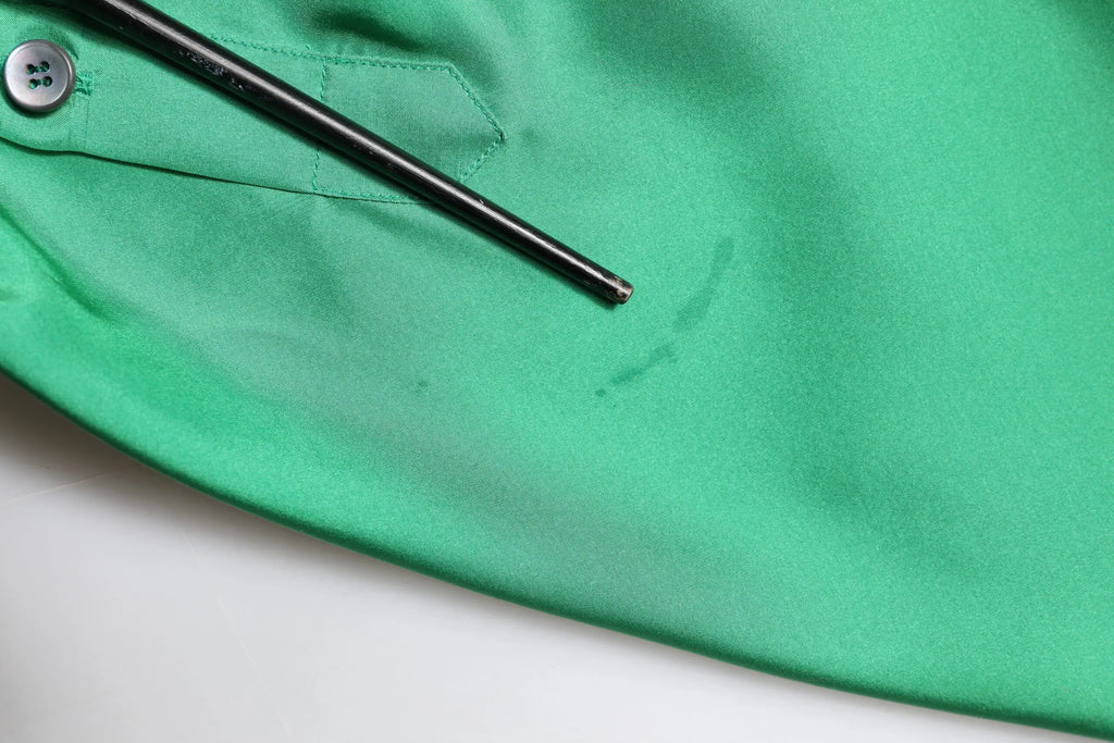 Un outil en métal noir à pointe repose sur la chemise décontractée en satin de soie verte dolce & gabbana à manches longues