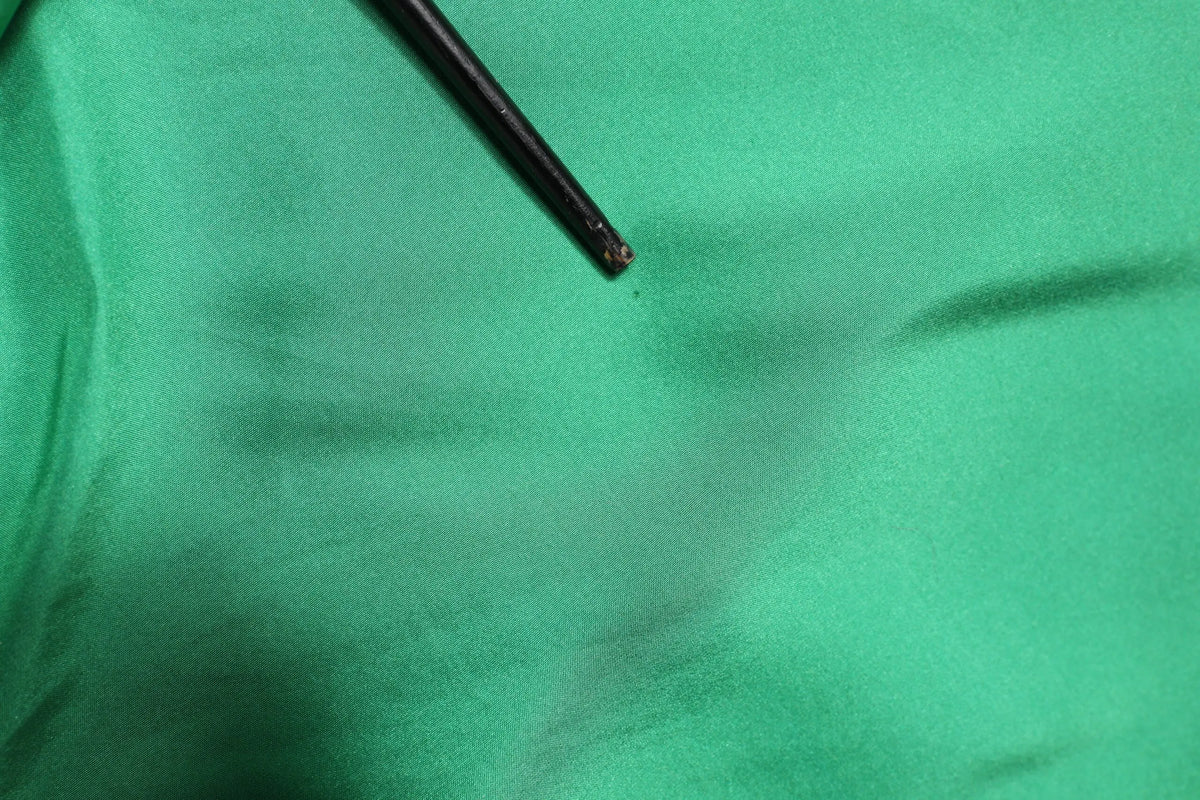 Un outil noir fin avec une pointe légèrement usée posé sur un tissu vert en soie satinée d’une chemise dolce & gabbana
