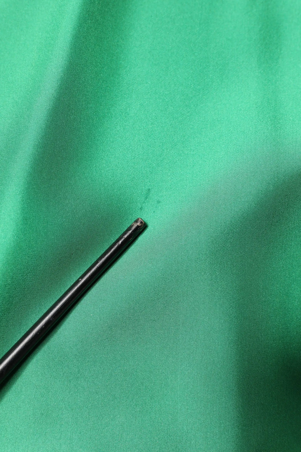 Pointe de stylo noire cylindrique reposant sur une chemise décontractée en satin de soie verte dolce & gabbana à manches longues