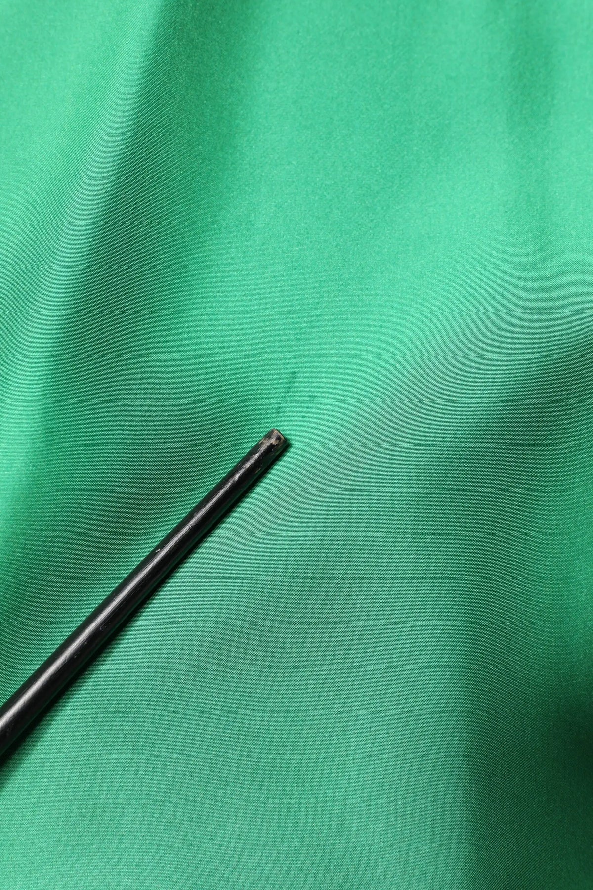 Pointe de stylo noire cylindrique reposant sur une chemise décontractée en satin de soie verte dolce & gabbana à manches longues
