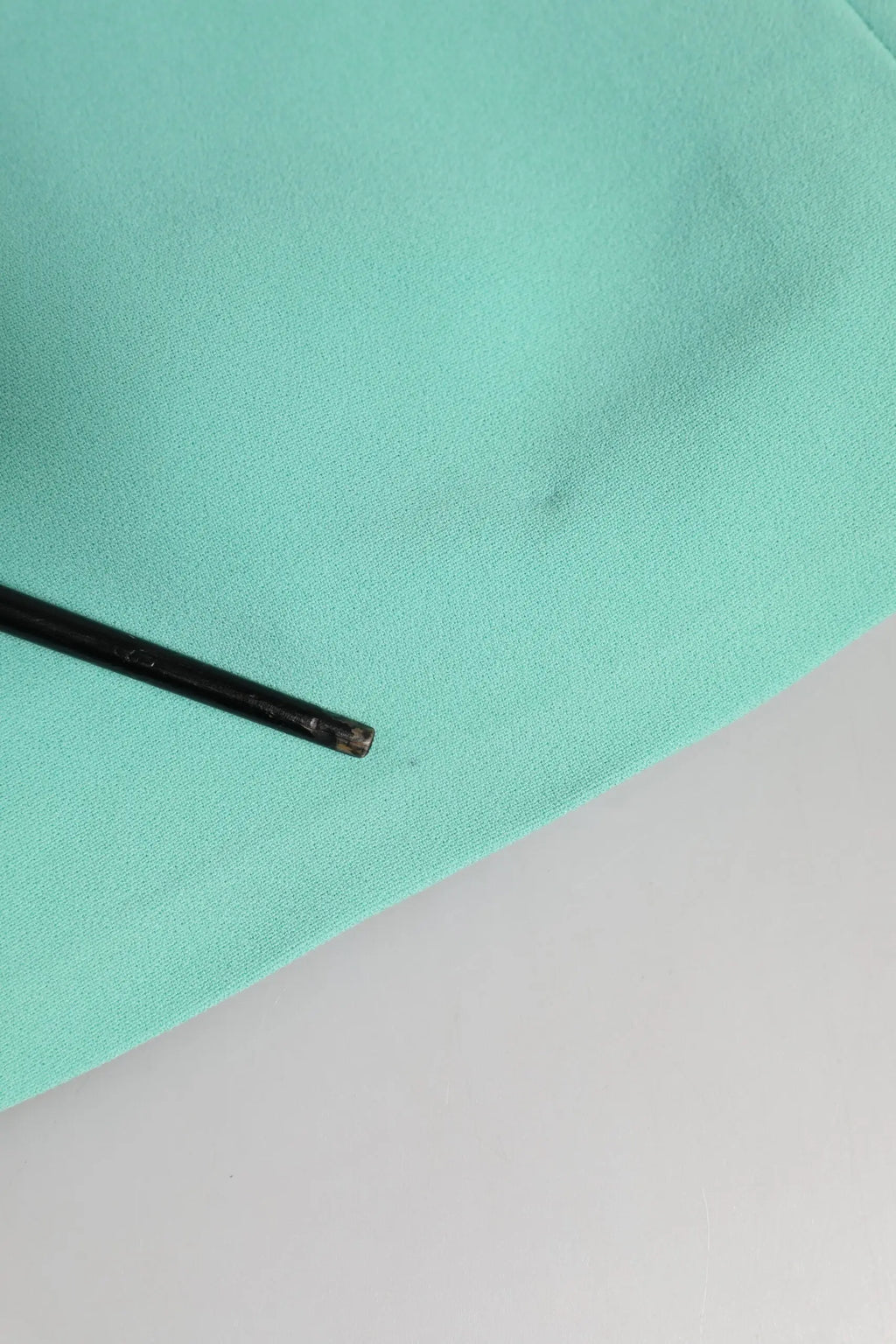 Un stylo noir élégant posé en diagonale sur un tissu vert menthe doux à côté d’une robe midi sans manches en viscose verte dolce & gabbana