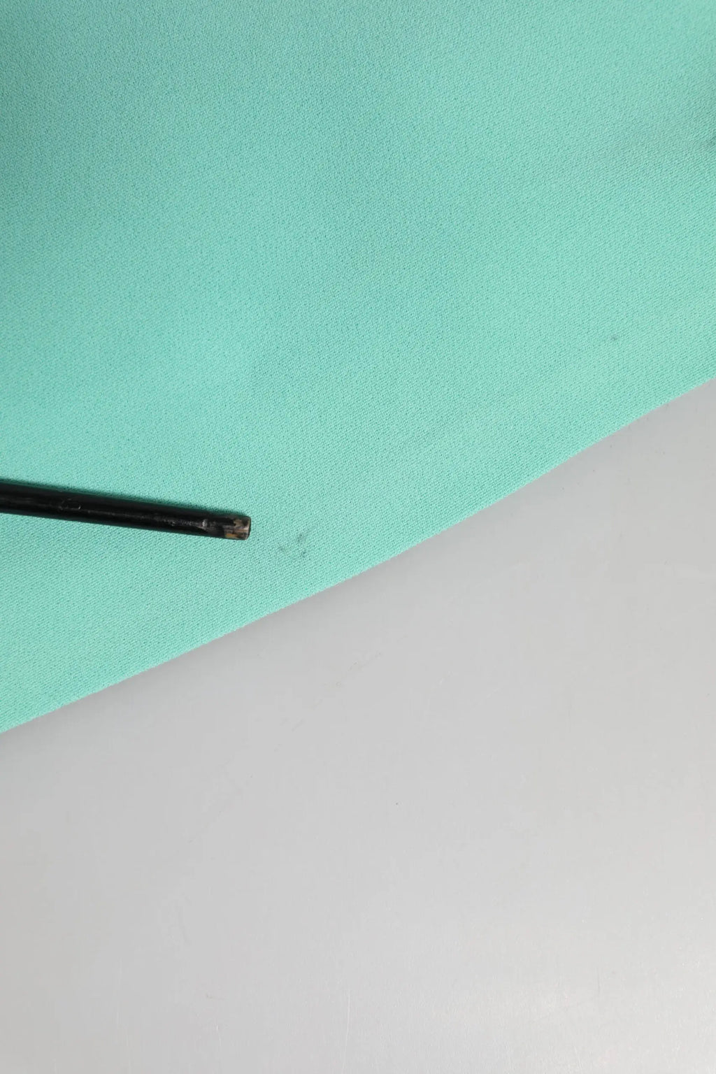 Un stylo noir mat élégant posé en diagonale sur un tissu teal doux à côté d’une robe fourreau midi sans manches en viscose verte dolce & gabbana