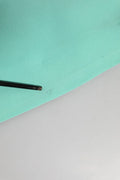 Un stylo noir mat élégant posé en diagonale sur un tissu teal doux à côté d’une robe fourreau midi sans manches en viscose verte dolce & gabbana