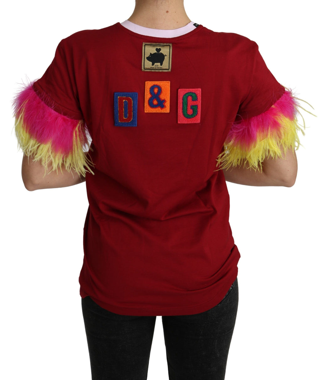 T-shirt Dolce & Gabbana rouge avec imprimé de cochon, manches en plumes et style décontracté visible sur l'image.