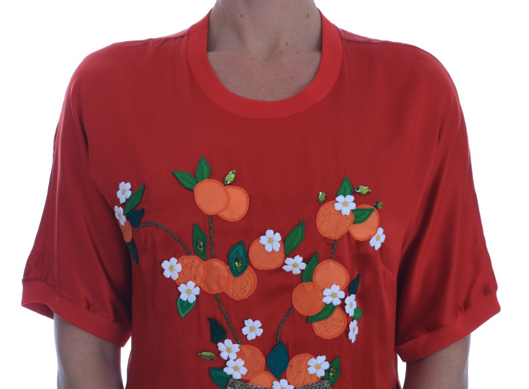 Blouse en soie rouge Dolce & Gabbana avec motifs d’oranges florales et détails en cristal, portée dans une image.