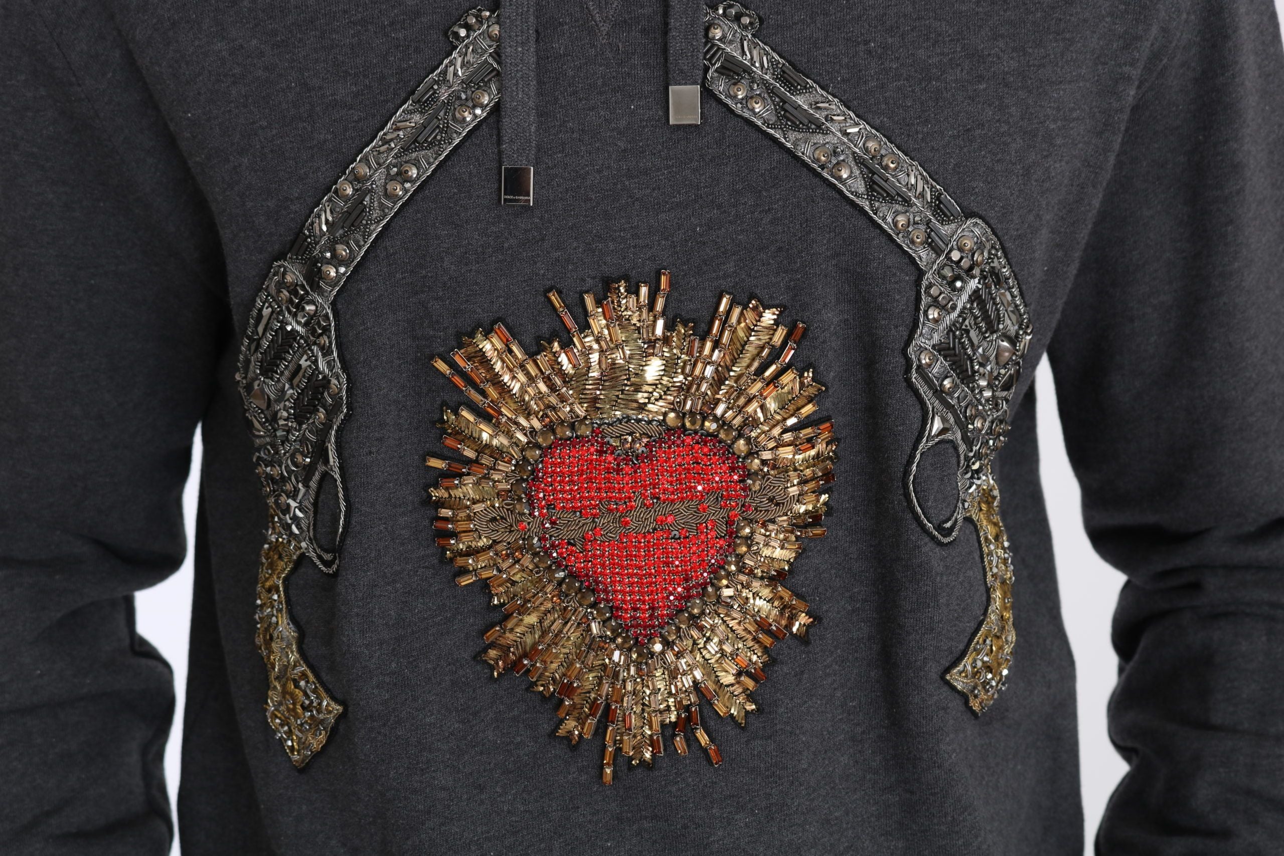 Pull gris à capuche Dolce & Gabbana avec cœur en cristal rouge et motif pistolet, vue de face.