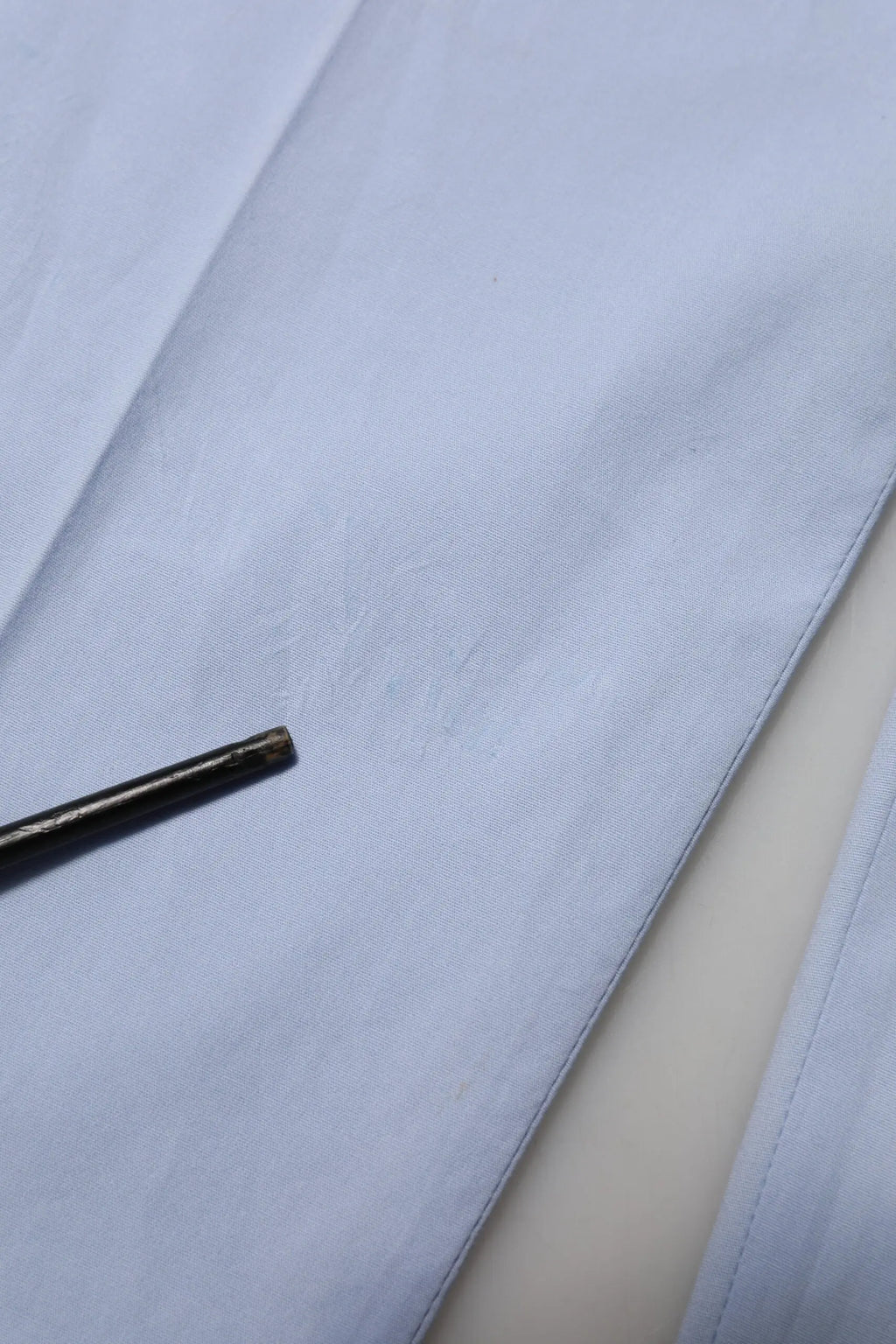 Un outil métallique fin et sombre posé sur un tissu bleu clair à côté d un pantalon homme dolce gabbana light blue coton stretch tapered