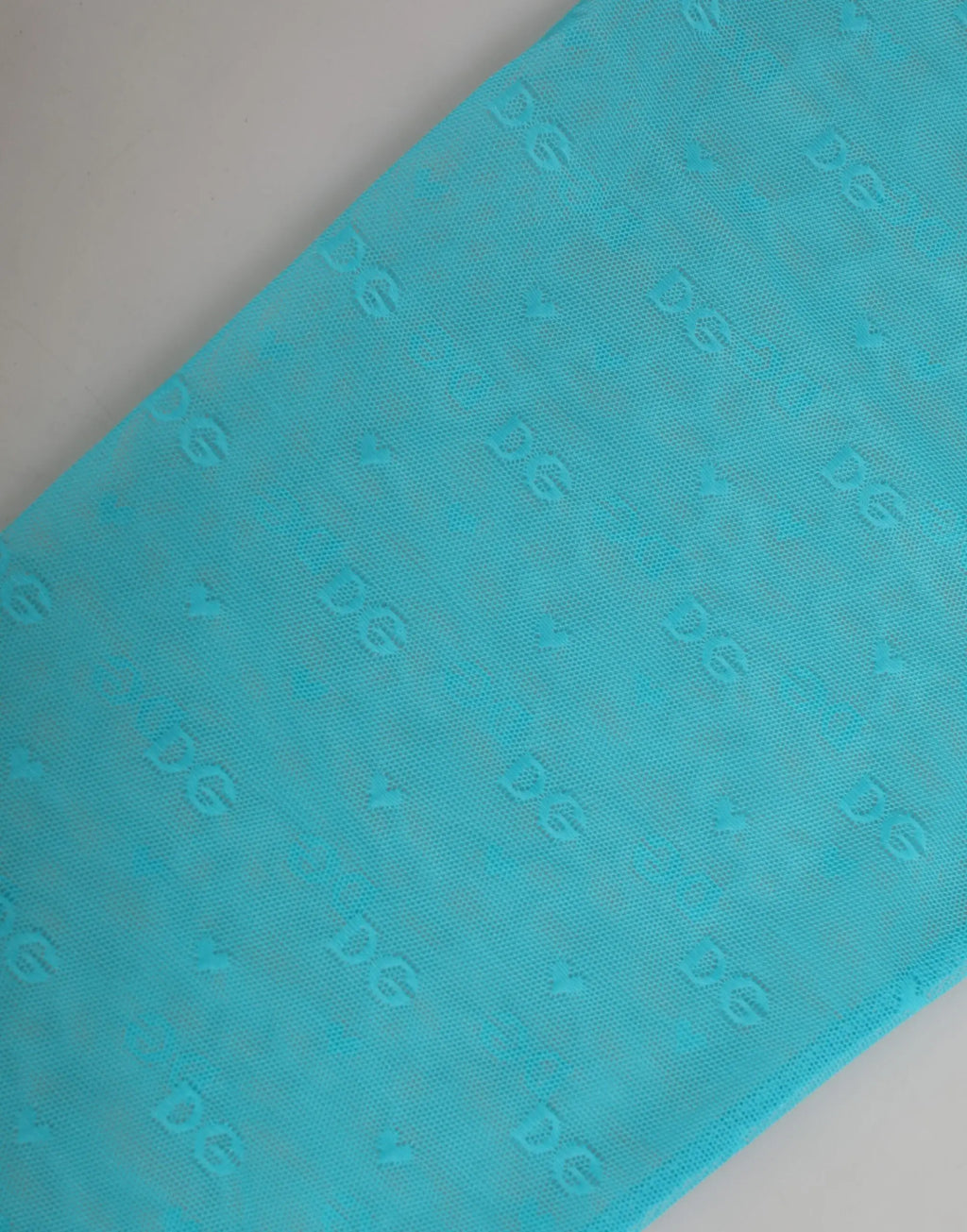 Foulard en tissu turquoise avec motif logo embossé subtil associé au pantalon moulant dentelle bleu clair dolce gabbana