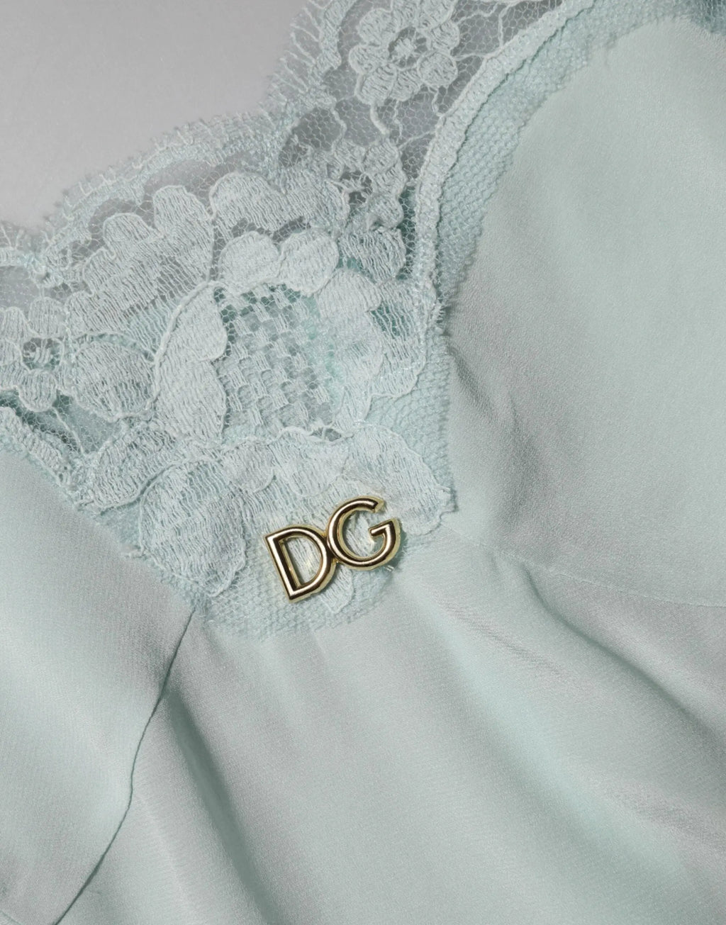 Une épingle délicate en or avec logo dg orne le tissu en dentelle vert menthe d’une robe midi bodycon en soie dolce & gabbana light blue