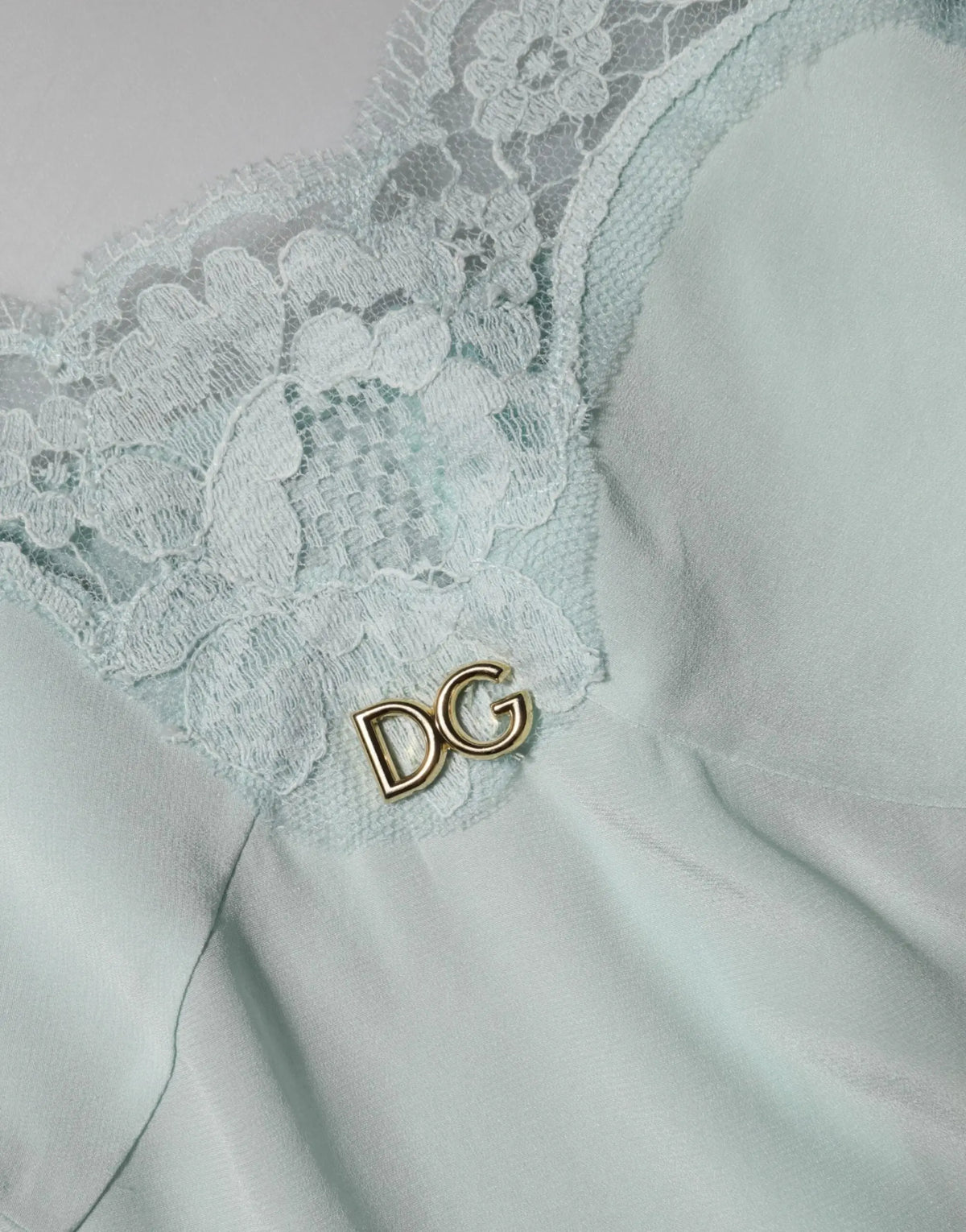 Une épingle délicate en or avec logo dg orne le tissu en dentelle vert menthe d’une robe midi bodycon en soie dolce & gabbana light blue
