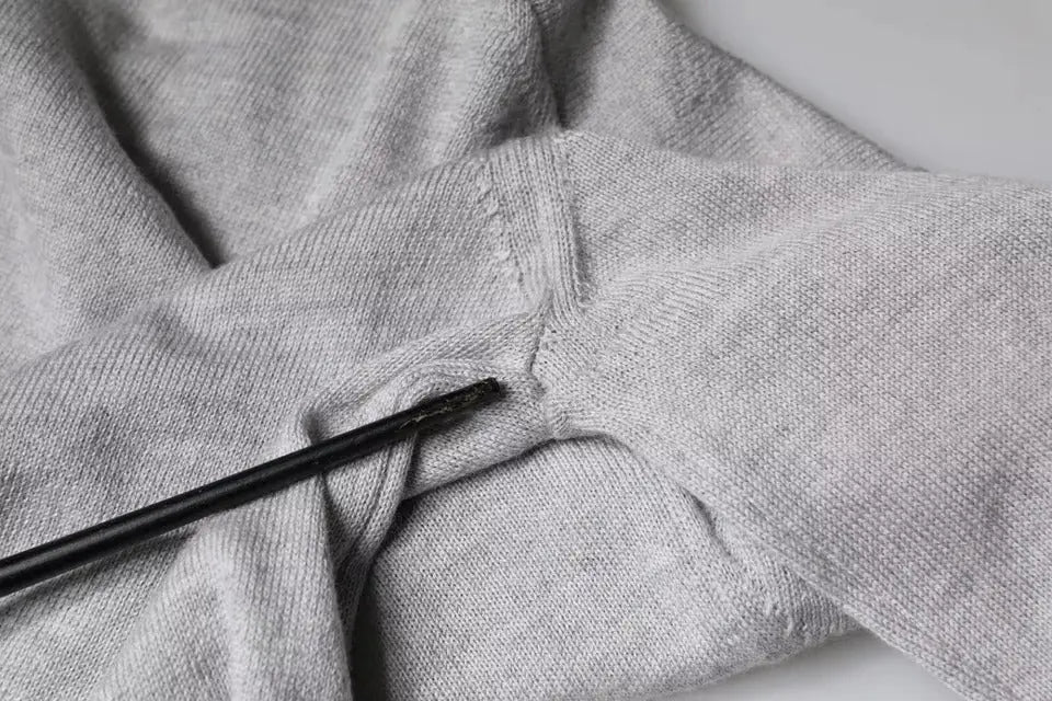 Un stylo noir texturé posé en diagonale sur le tissu gris clair en laine douce d un pull dolce gabbana col rond