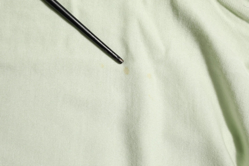 Un tournevis noir et fin posé en diagonale sur un pull dolce & gabbana à col roulé vert clair en tissu texturé