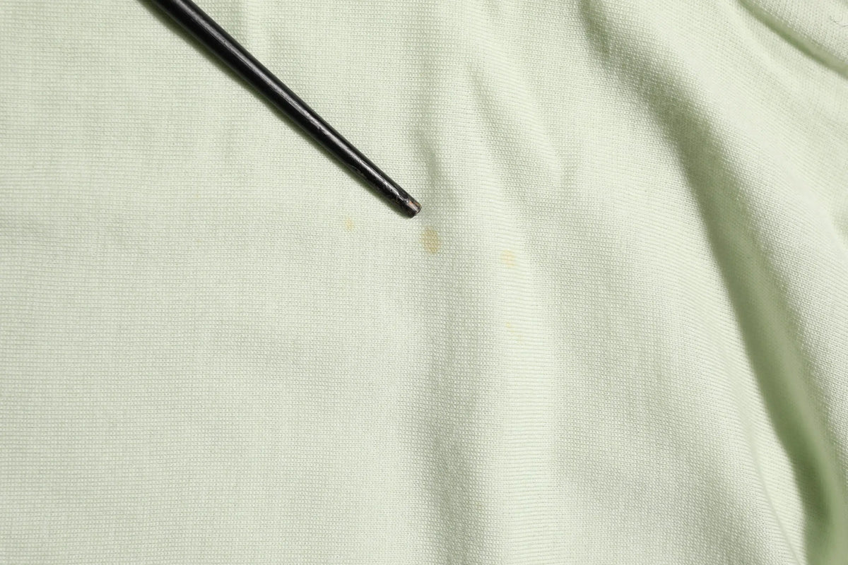 Un tournevis noir et fin posé en diagonale sur un pull dolce & gabbana à col roulé vert clair en tissu texturé