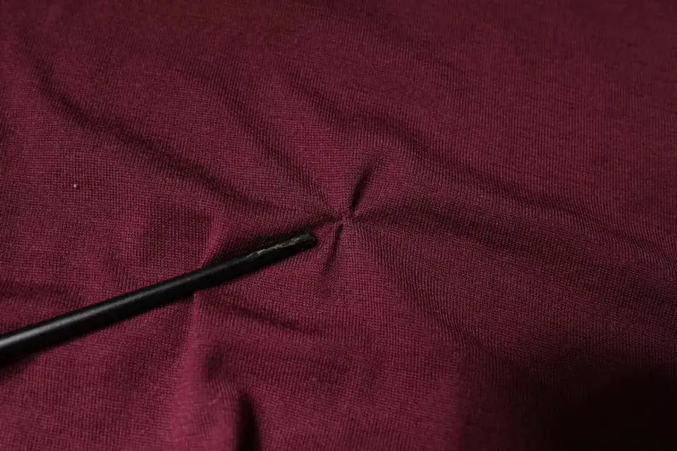 Un stylo noir posé sur un tissu texturé bordeaux avec un pull en cachemire dolce & gabbana col v homme