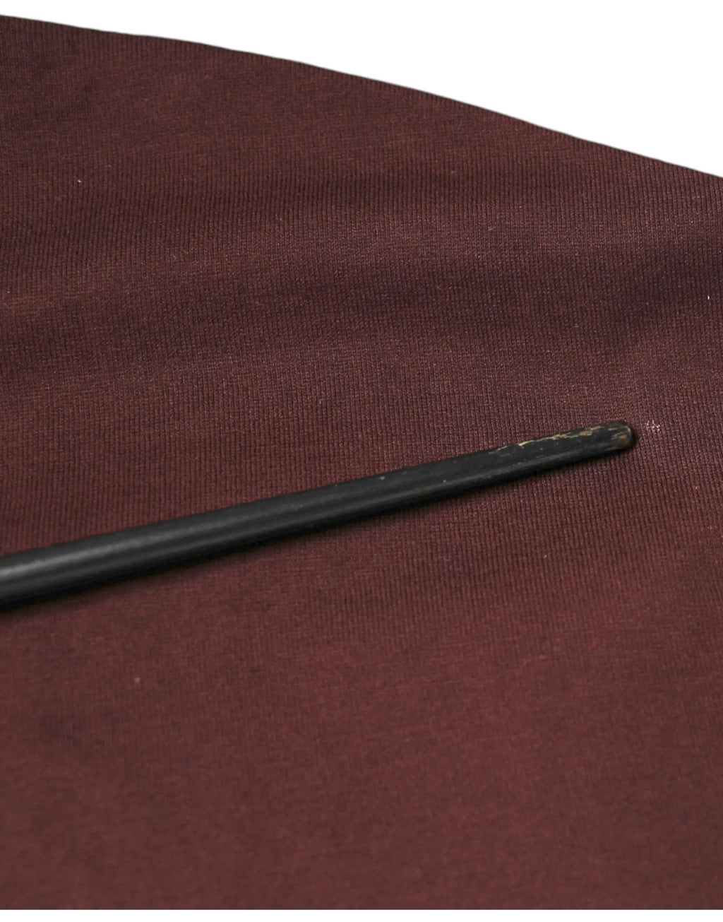 Une baguette noire élégante avec une pointe arrondie repose en diagonale sur un t-shirt coton dolce & gabbana maroon dg logo col rond