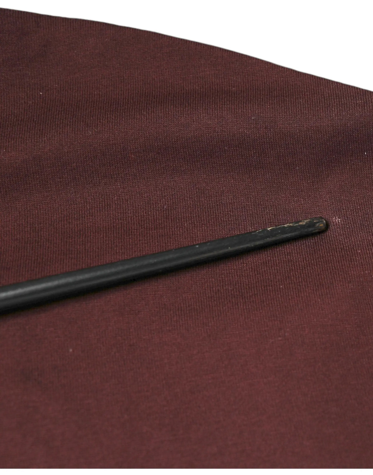 Une baguette noire élégante avec une pointe arrondie repose en diagonale sur un t-shirt coton dolce & gabbana maroon dg logo col rond