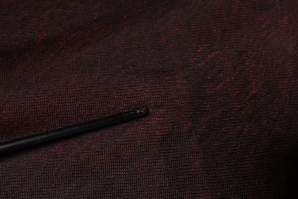 Black crochet hook resting on textured deep maroon polyester fabric of dolce & gabbana crew neck pullover sweater