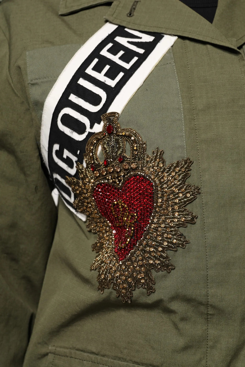 Broche en forme de coeur rouge avec ornement doré et couronne sur manteau militaire vert dolce & gabbana