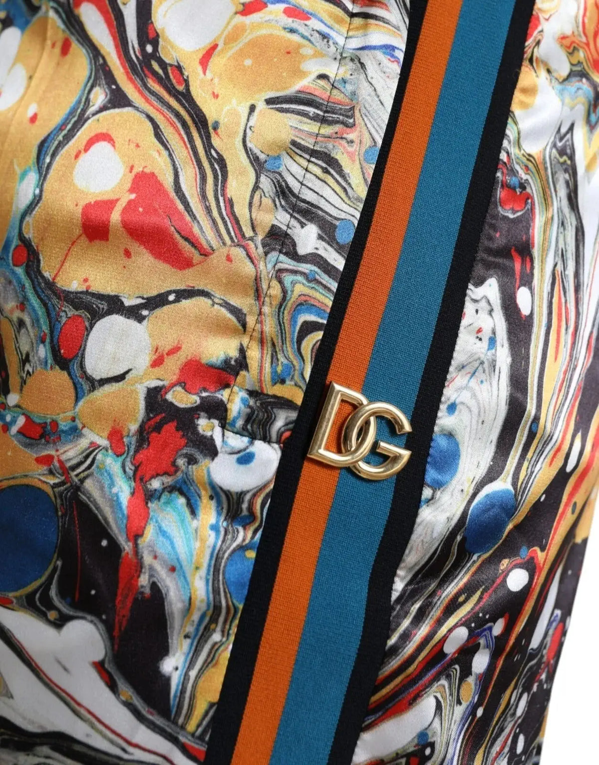 Une boucle logo dg dorée orne un pantalon dolce & gabbana en satin multicolore à motifs marbrés jaunes rouges bleus et noirs