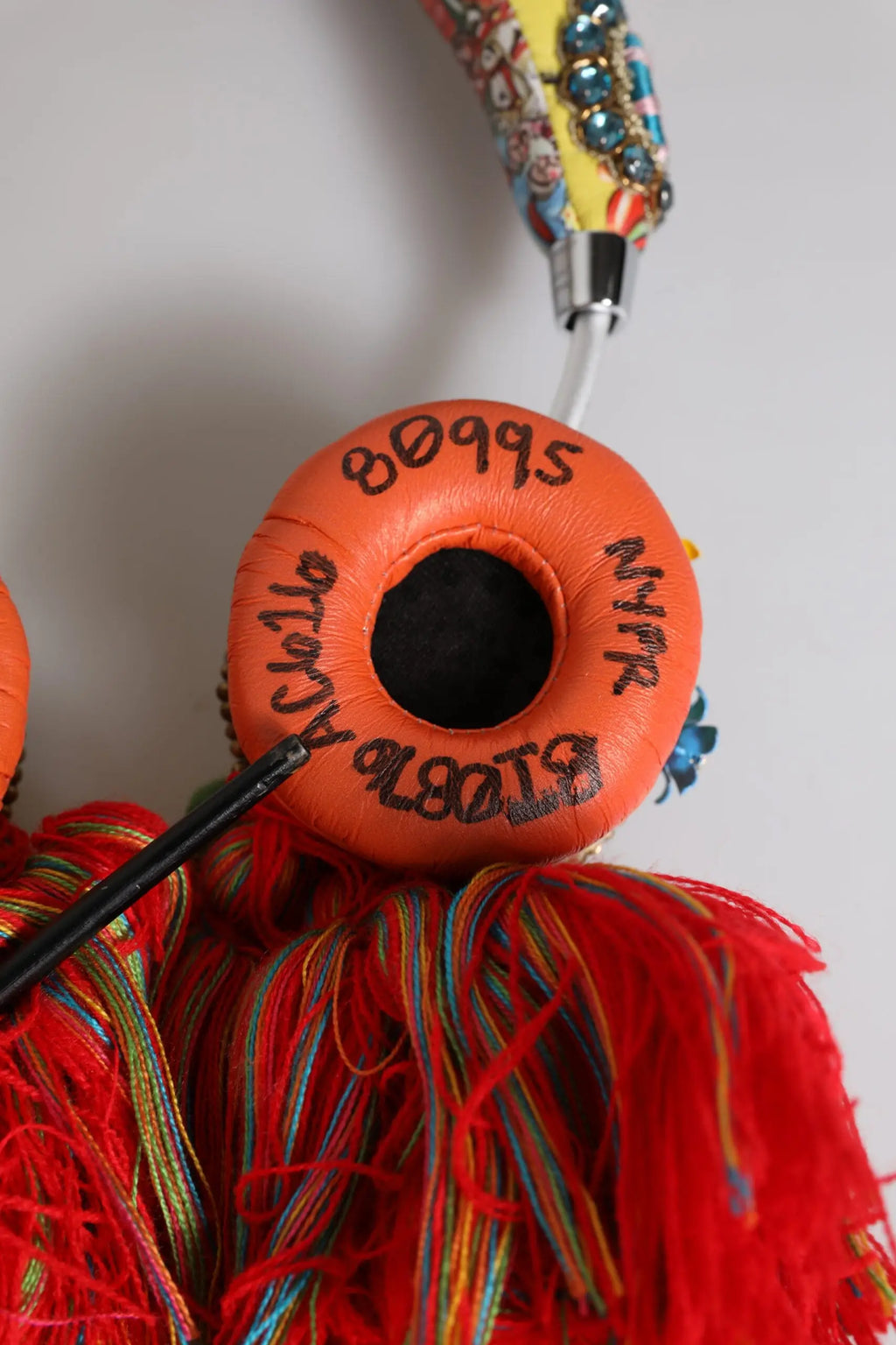 Écouteurs circulaires orange dolce & gabbana avec texte manuscrit noir et pompons multicolores fantaisistes