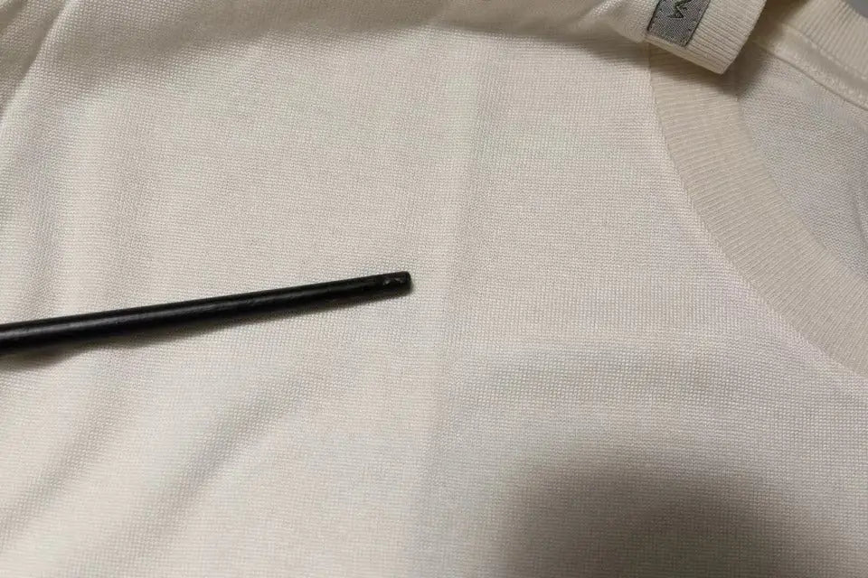 Crochet noir posé sur un tissu blanc texturé à côté d un t shirt dolce gabana en soie blanc cassé à manches courtes col rond