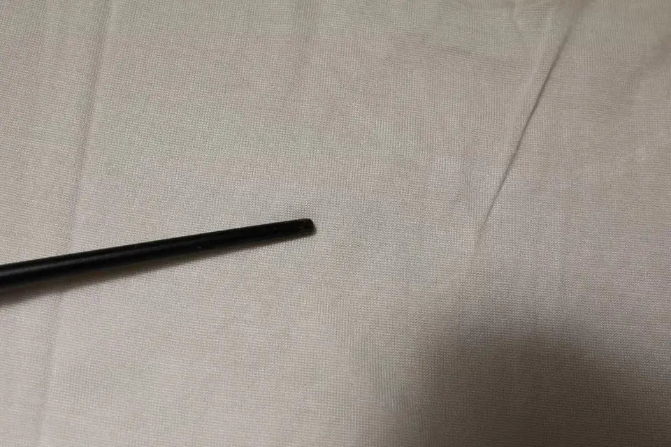 Objet cylindrique noir mat posé en diagonale sur tissu blanc texturé avec t shirt dolce & gabbana off white soie col rond manches courtes