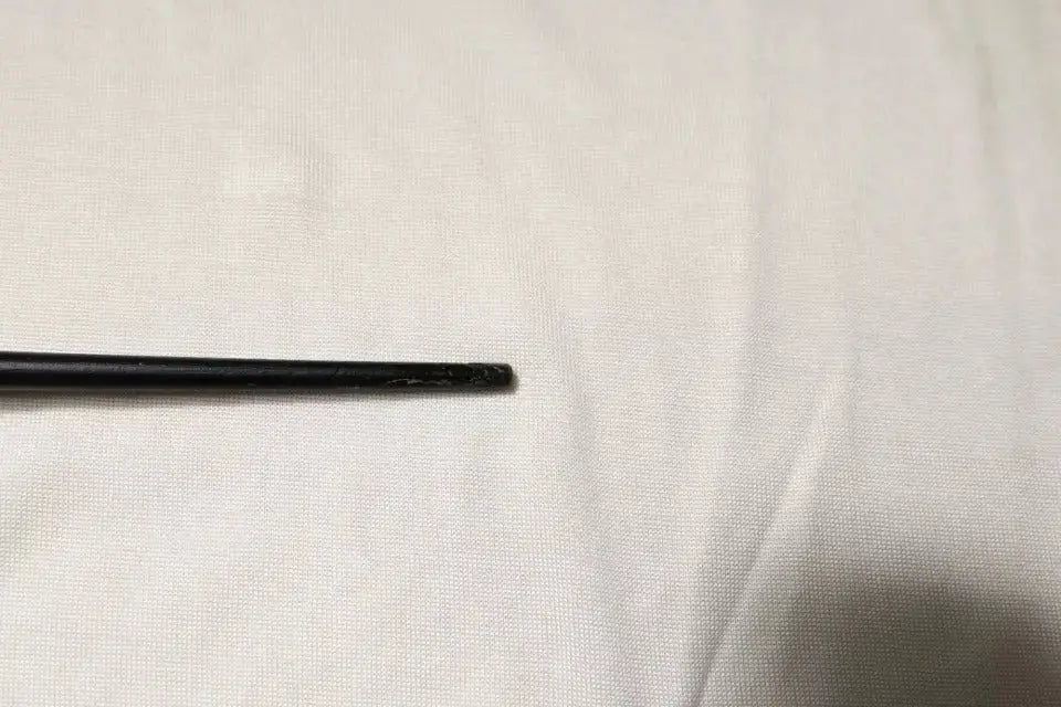 Objet cylindrique noir avec extrémité légèrement usée reposant sur tissu clair à côté d’un t-shirt dolce & gabbana en soie blanche crème