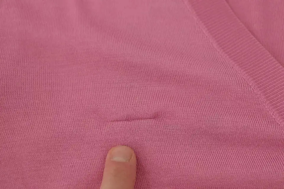 Un doigt pointe une petite pliure sur un cardigan dolce & gabbana rose en maille côtelée 100% soie