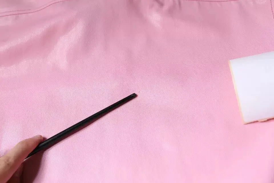 Main tenant une baguette noire sur un tissu rose du chemisier dolce & gabbana en coton rose à col boutonné