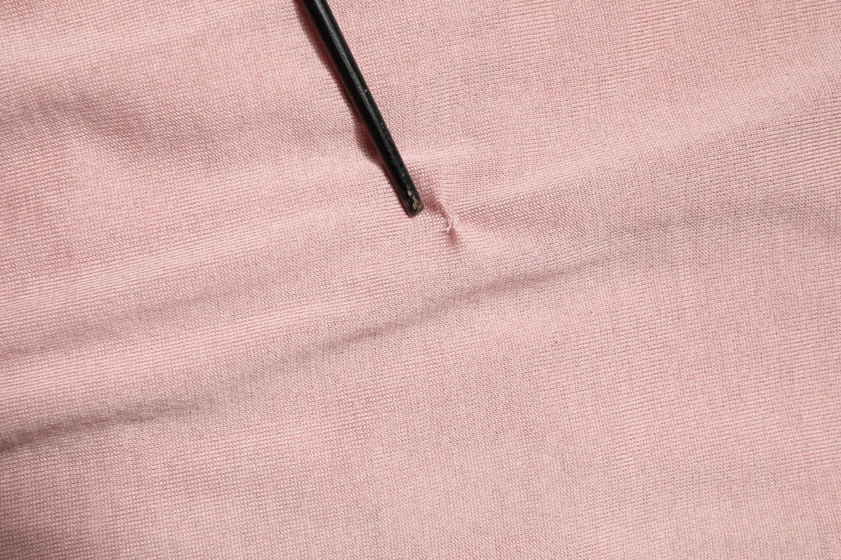 Un stylo noir posé en diagonale sur un tissu rose doux en maille du cardigan dolce & gabbana avec dentelle fleurie