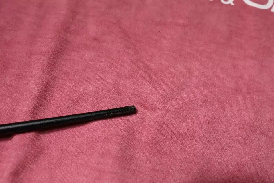 Objet cylindrique noir légèrement usé posé sur tissu rose d un t shirt dolce & gabbana en coton à col rond avec logo rose