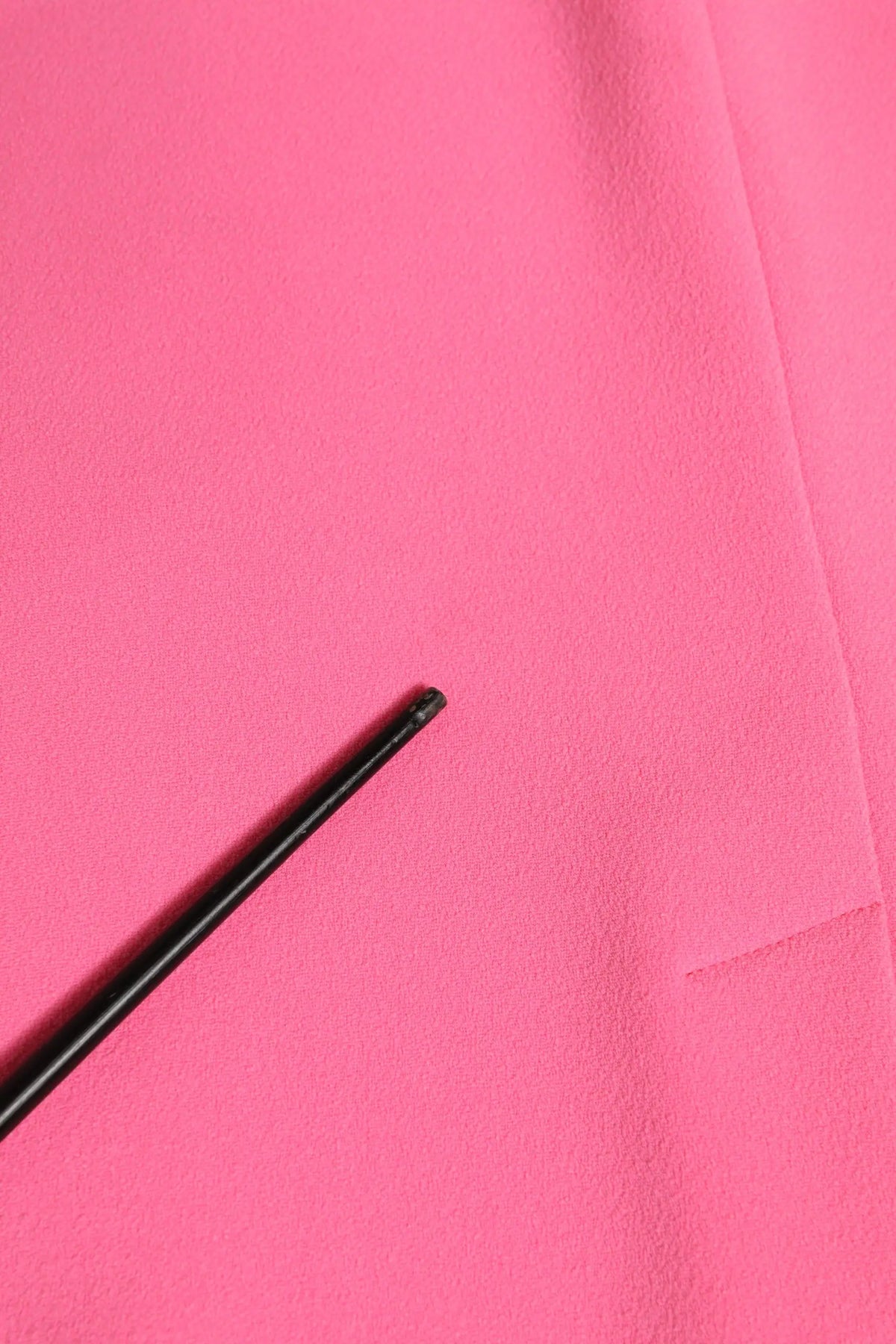 Un stylo noir mat élégant repose en diagonale sur une robe midi fourreau en polyester rose de dolce & gabbana manches longues