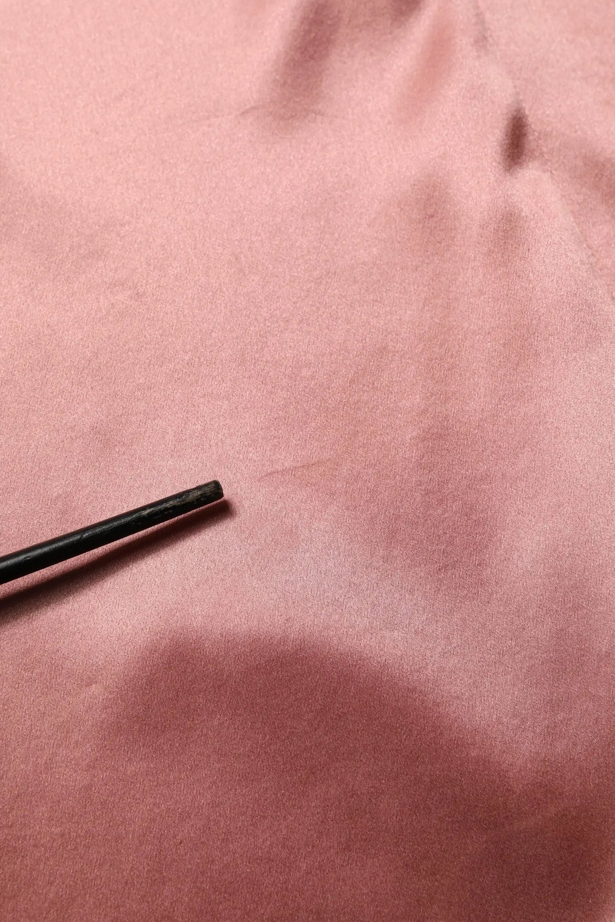 Un crayon cylindrique noir reposant sur un tissu rose doux du chemisier en satin soie rose v neck à manches longues dolce & gabbana