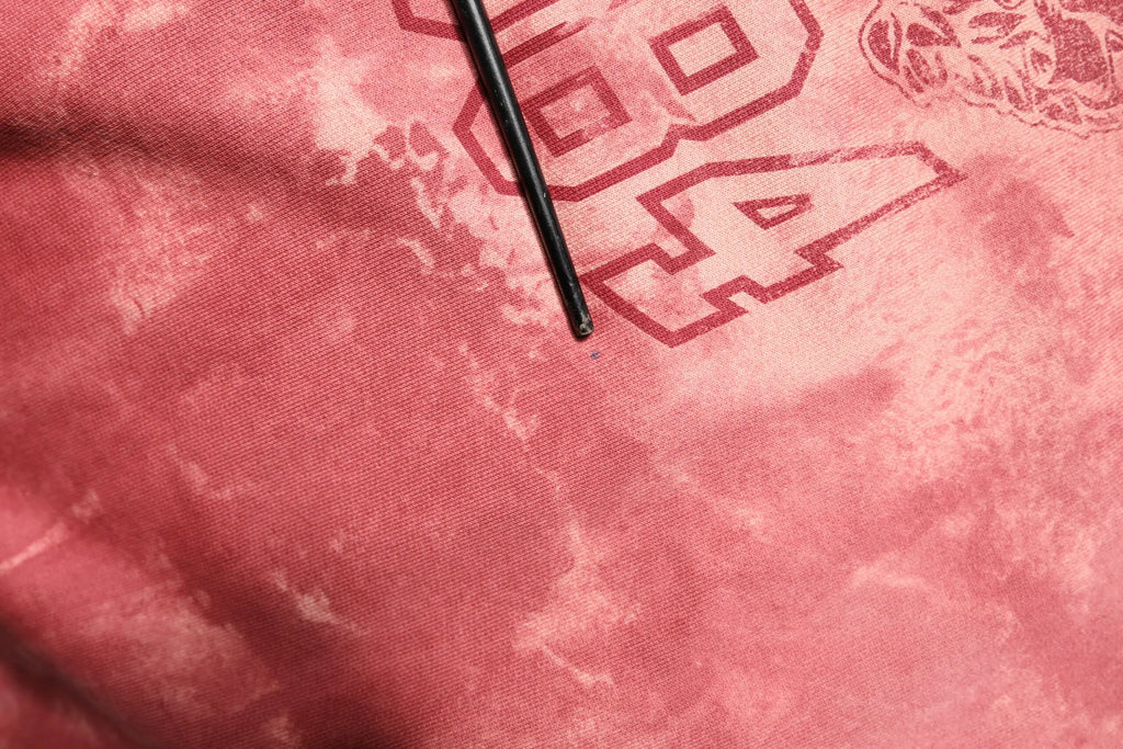 Stylo noir posé sur un tissu tie-dye rose avec lettrage rouge sur le sweat à capuche dolce & gabbana dg milano rose