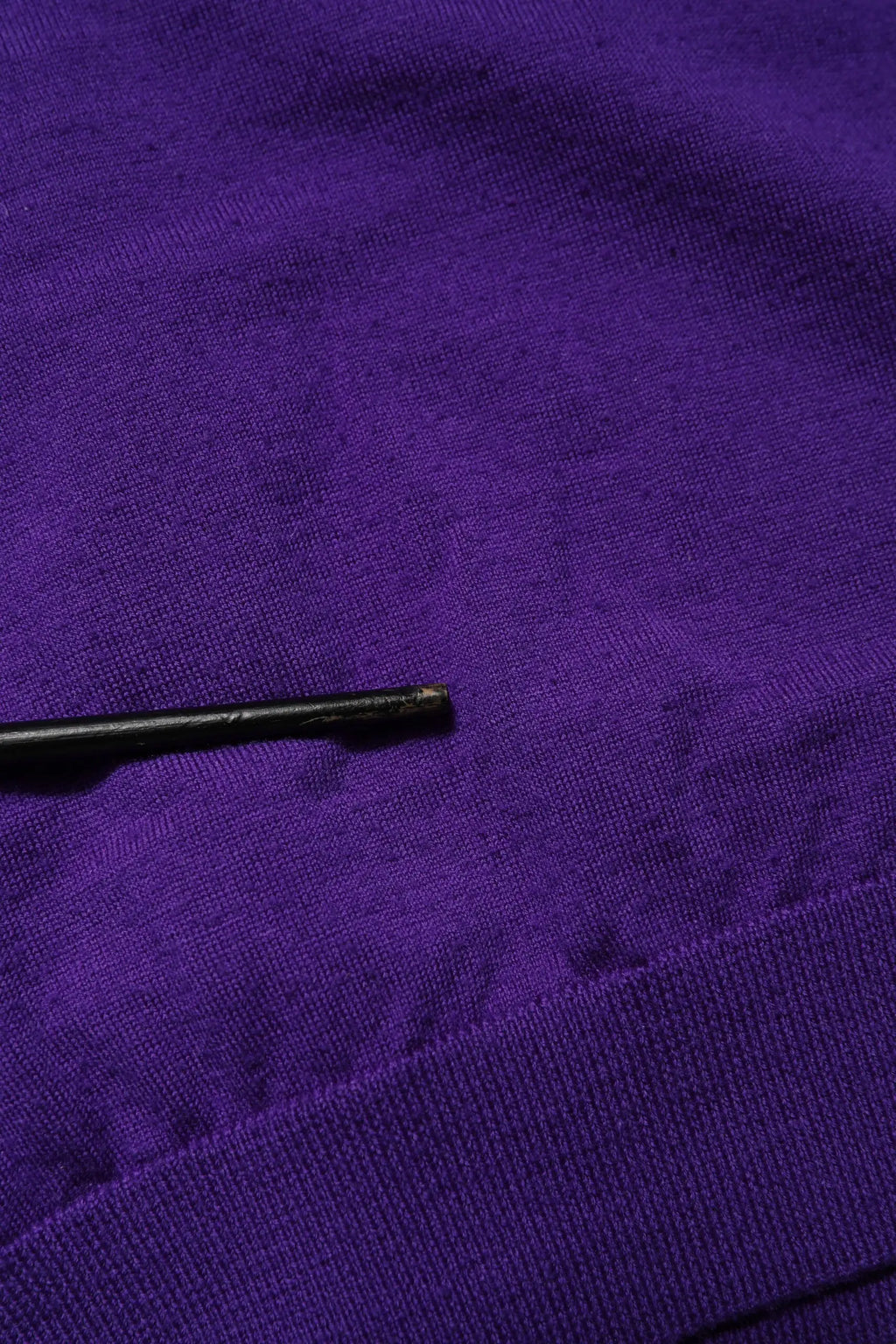 Un stylo noir mince posé en diagonale sur un tissu violet texturé avec un cardigan dolce & gabbana en laine tricotée col en v