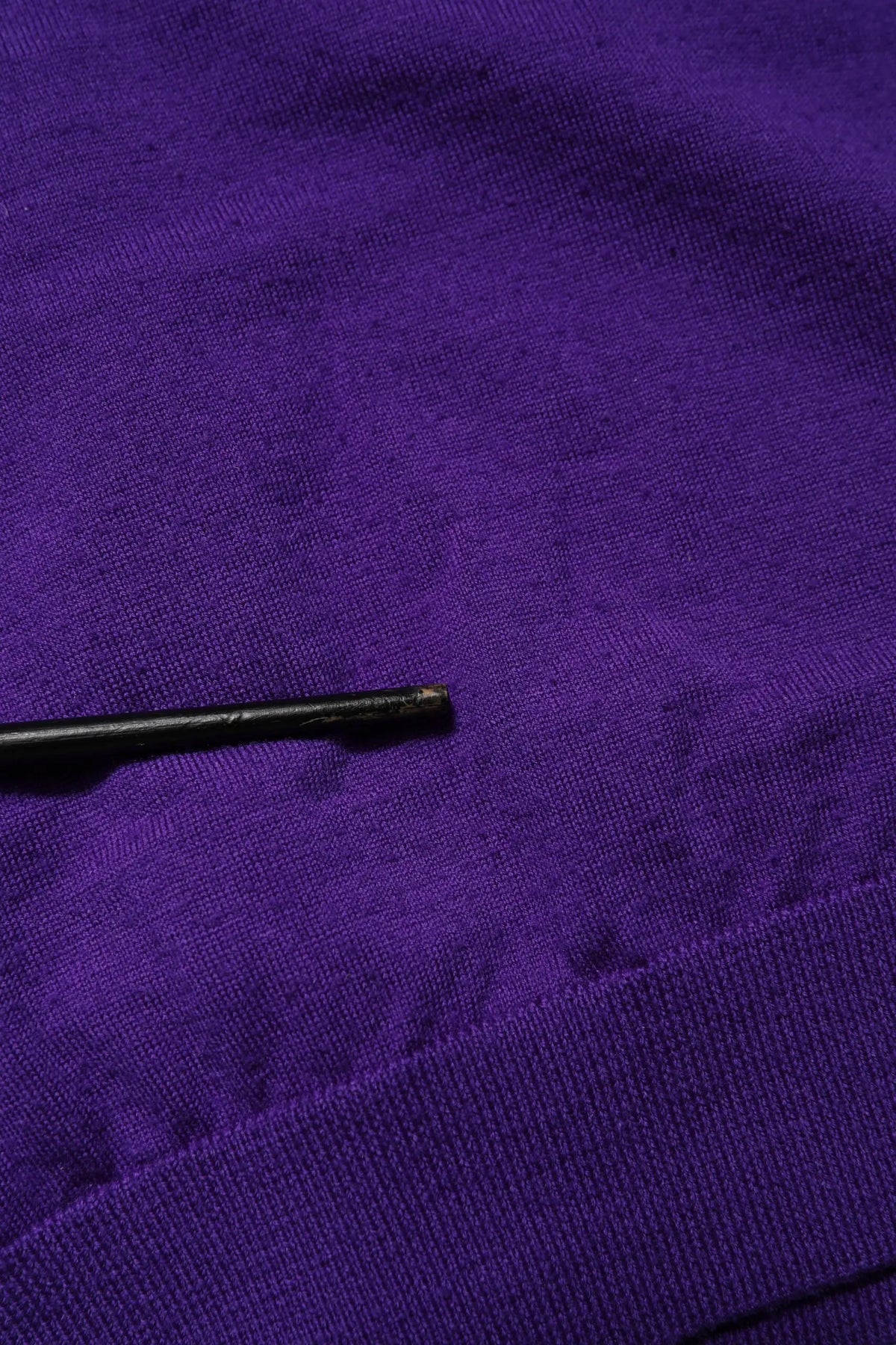 Un stylo noir mince posé en diagonale sur un tissu violet texturé avec un cardigan dolce & gabbana en laine tricotée col en v