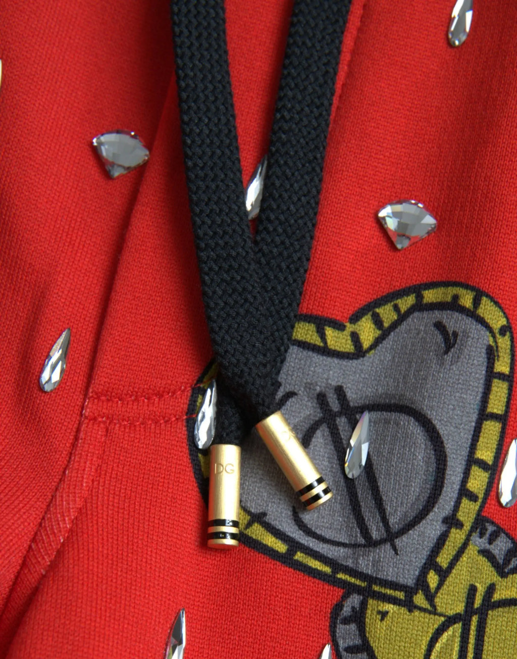 Cordon noir avec embouts métalliques dorés et logo dc attaché à un sweat à capuche rouge dolce & gabbana orné de strass argentés et d’un graphique cartoon