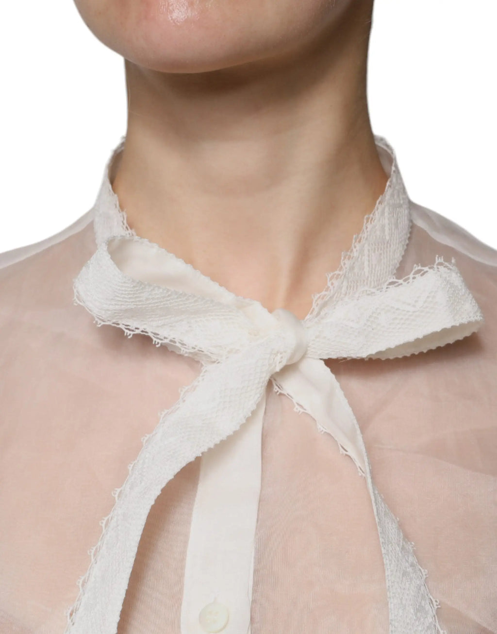 Un délicat nœud papillon en dentelle blanche à bord effiloché noué au col dun chemisier transparent dolce & gabbana