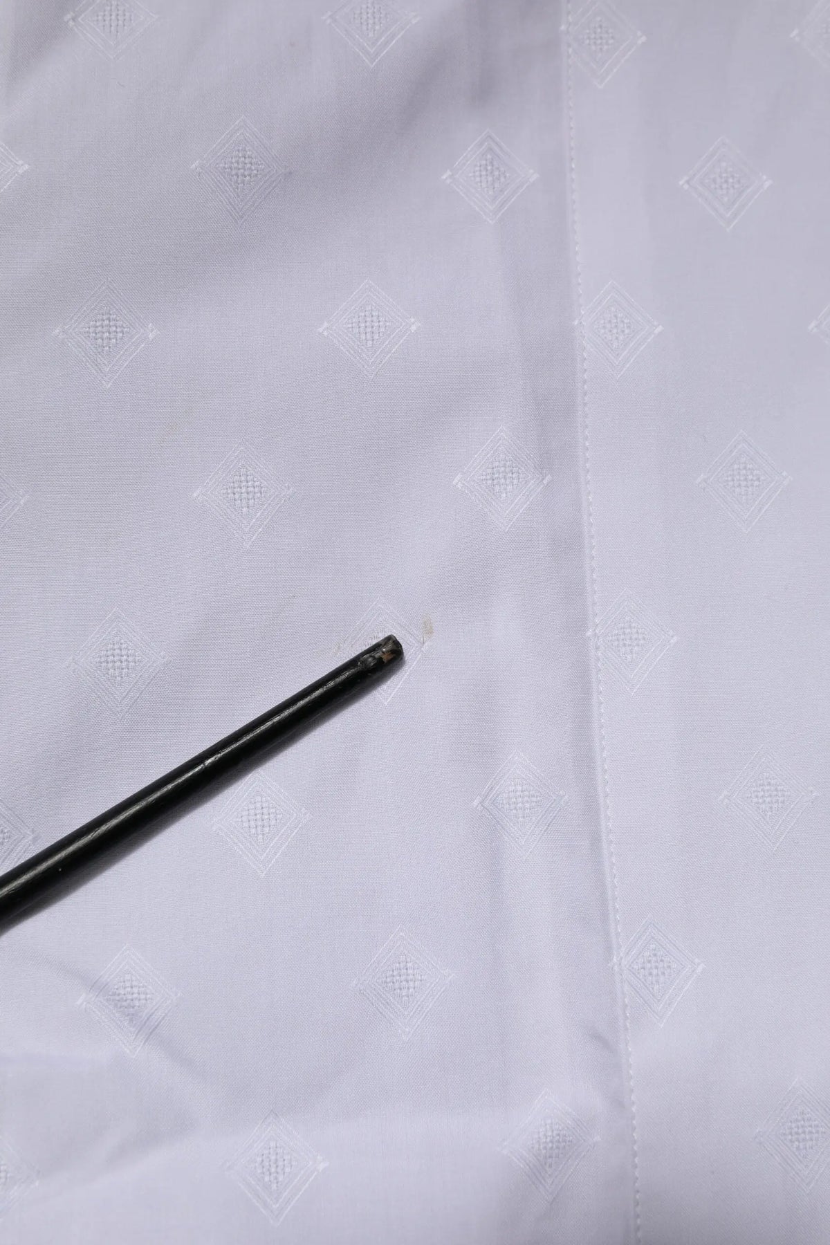 Objet cylindrique noir avec extrémité texturée légèrement usée sur tissu blanc du chemisier en popeline coton blanc dolce gabbana gold