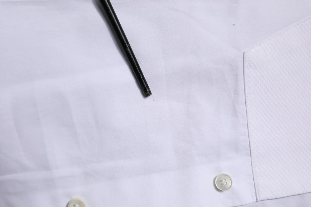 Un crayon noir repose en diagonale sur une chemise formelle blanche dolce gabbana en popeline de coton avec plis subtils