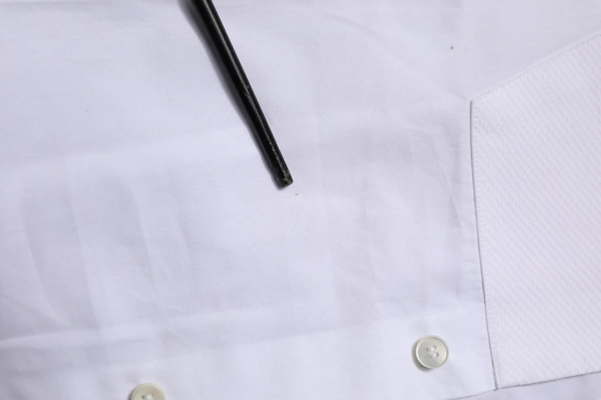 Un crayon noir repose en diagonale sur une chemise formelle blanche dolce gabbana en popeline de coton avec plis subtils