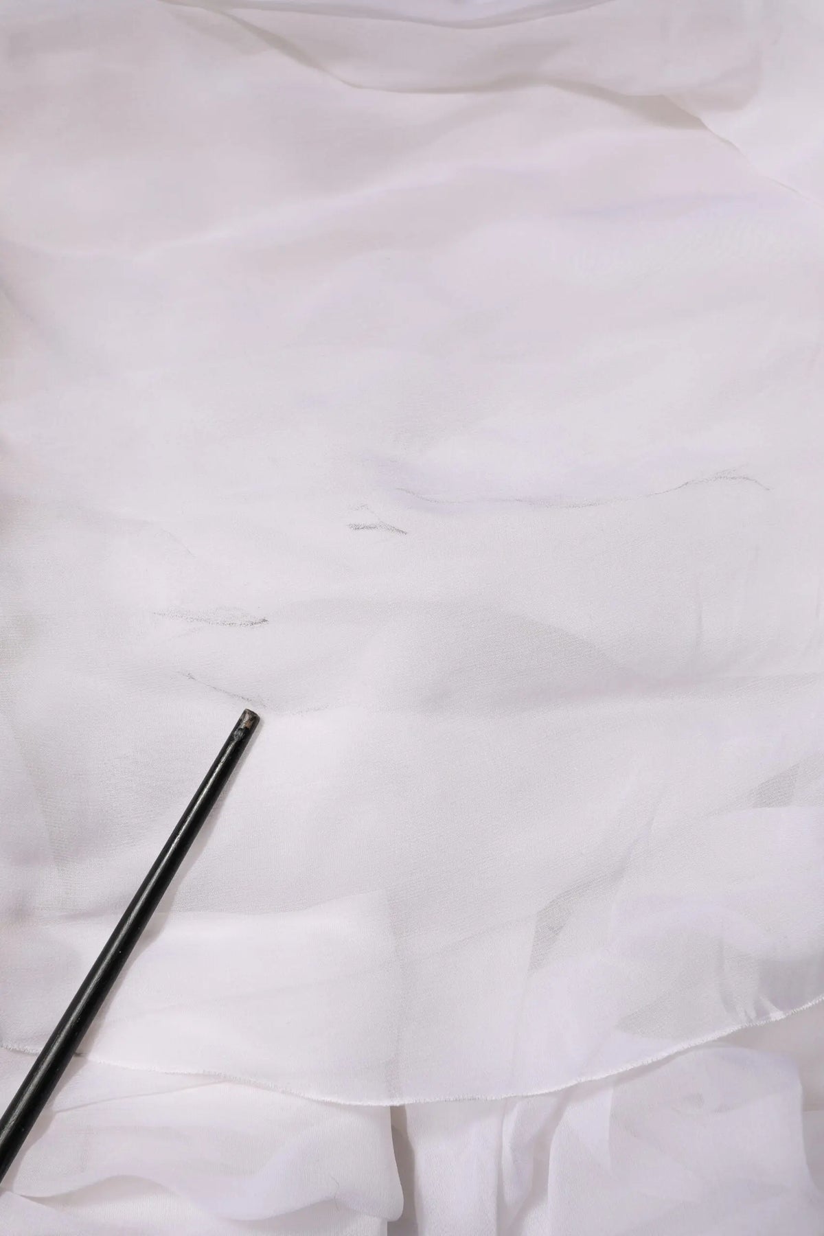 Un crayon noir élégant repose en diagonale sur un tissu blanc doux à côté d un bustier corset cropped en chiffon blanc dolce & gabbana