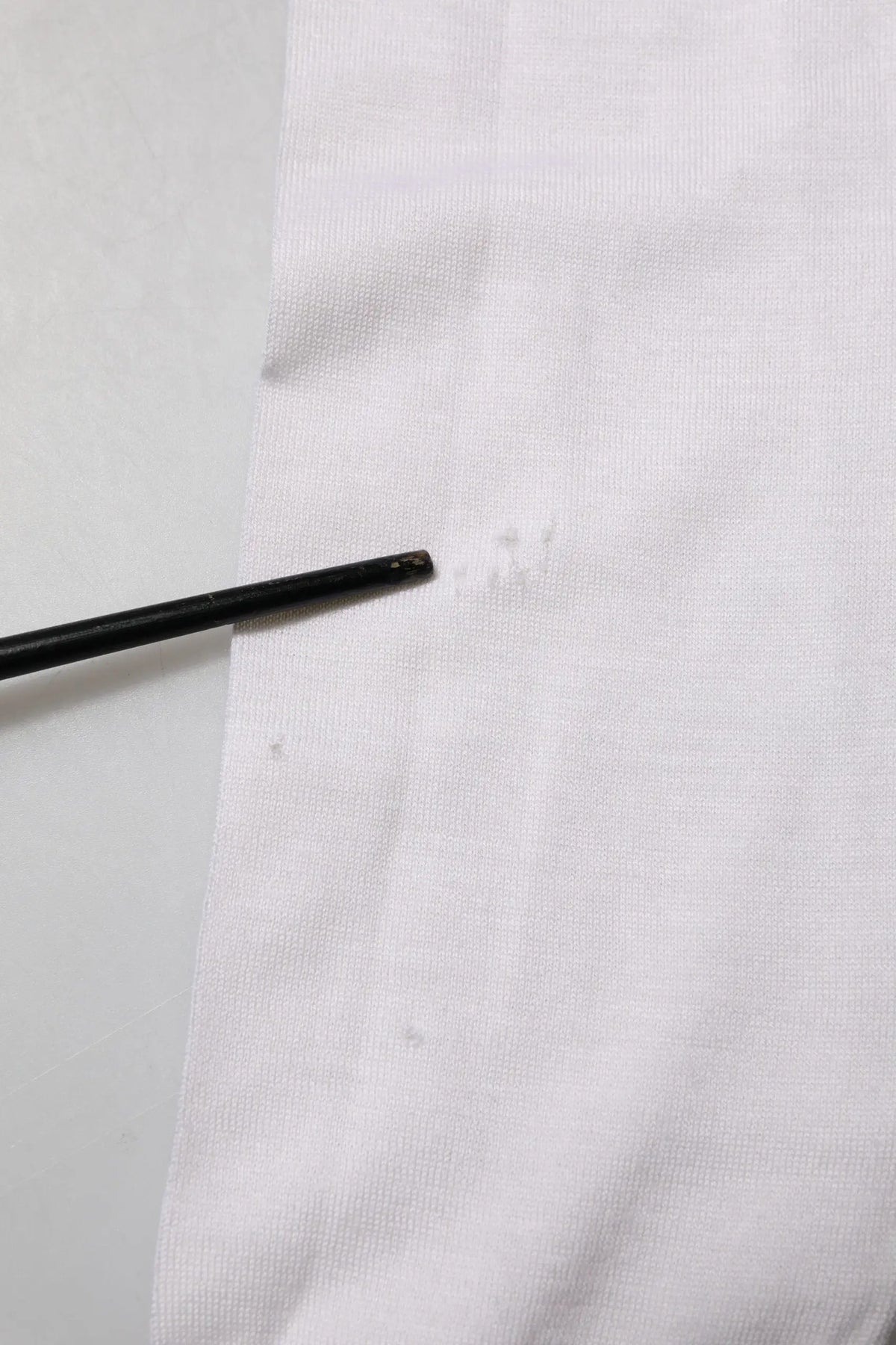 Outil cylindrique noir posé sur tissu blanc avec pull en cachemire blanc dolce & gabbana col en v logo