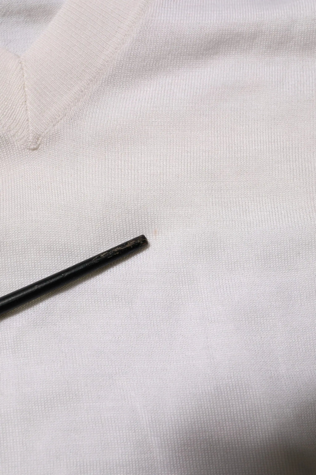 Objet cylindrique noir posé sur tissu blanc texturé avec pull dolce & gabbana en cachemire blanc col en v logo